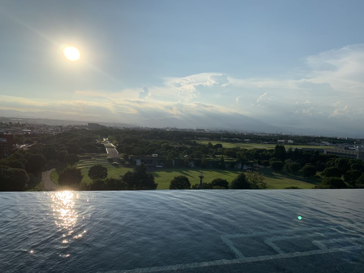 The rooftop infinity pool at SORANO HOTEL at sunset, its water edge seeming to merge with the view over Showa Kinen Park and the Tachikawa skyline